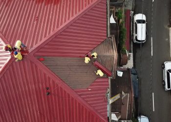 Aerial view of workers repairing a red metal roof in Quezon City, Philippines.